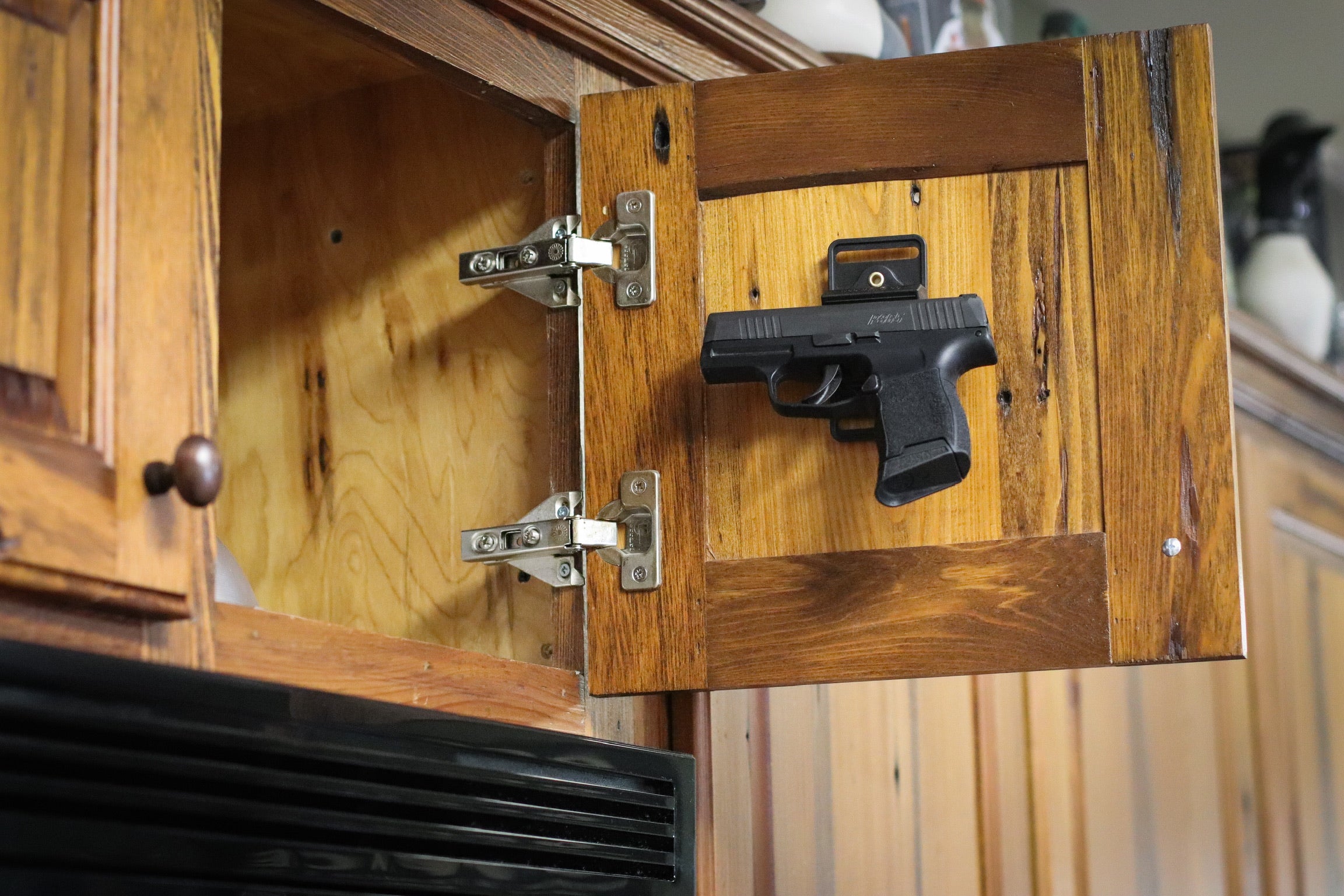 A pistol held by a CoJo magnetic mount inside a cabinet door